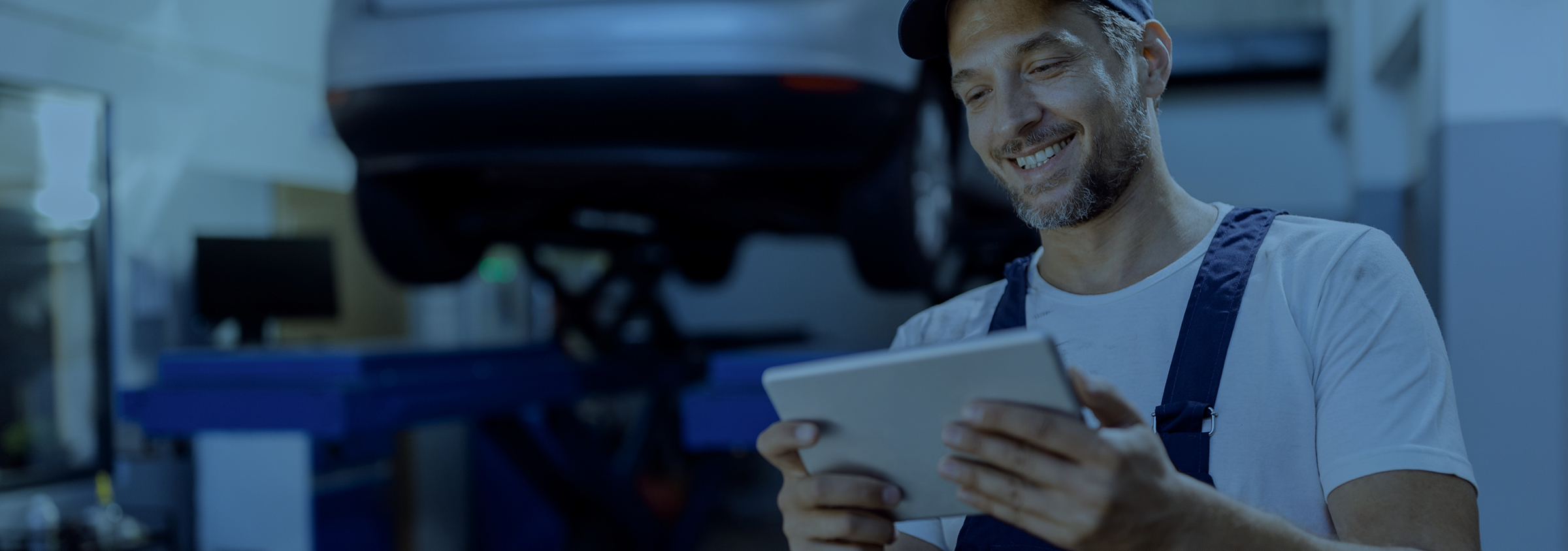 Smiling mechanic in the workshop apparently subscribes for a newsletter with his tablet